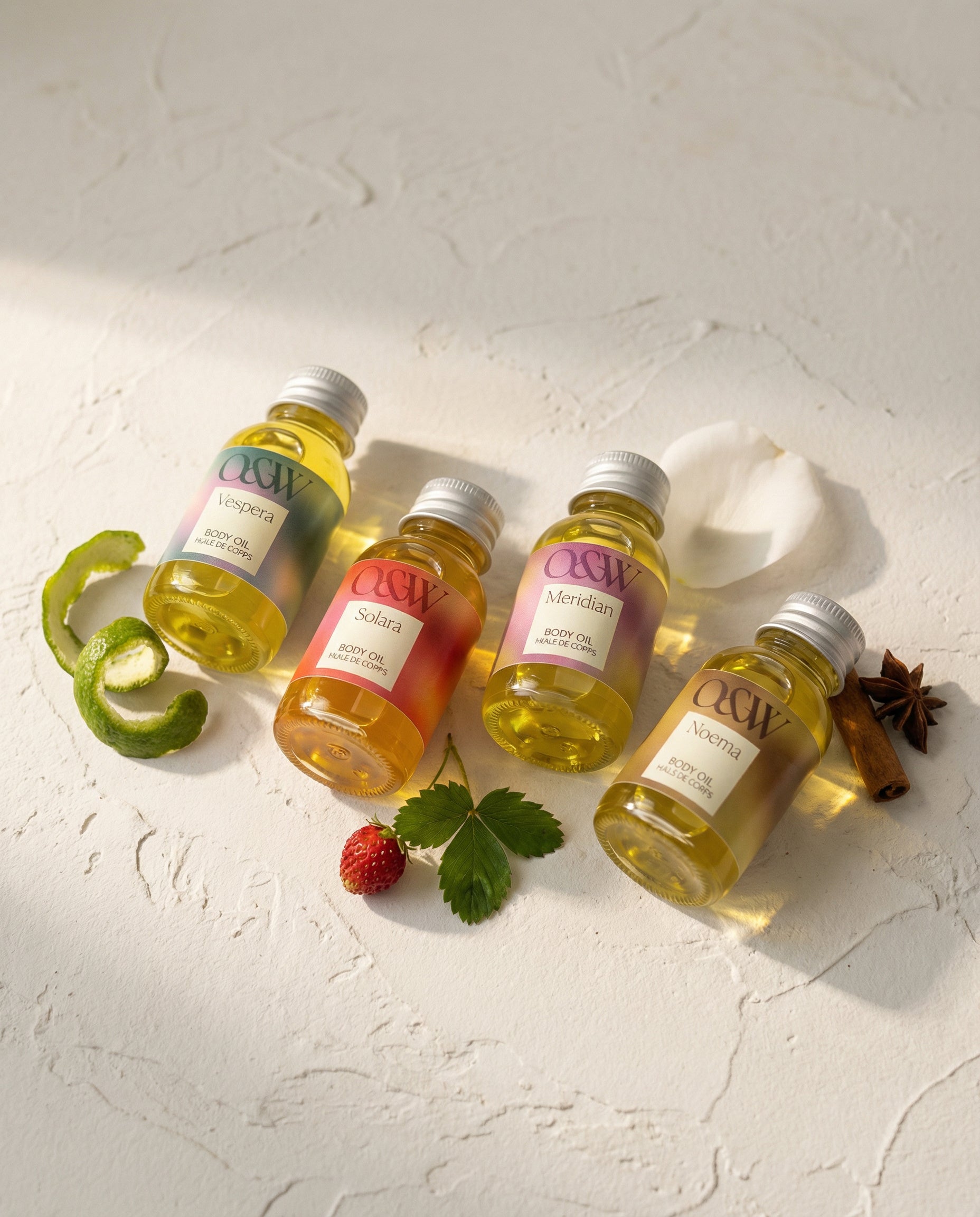 Four bottles of body oil with decorative scent notes on a textured white surface